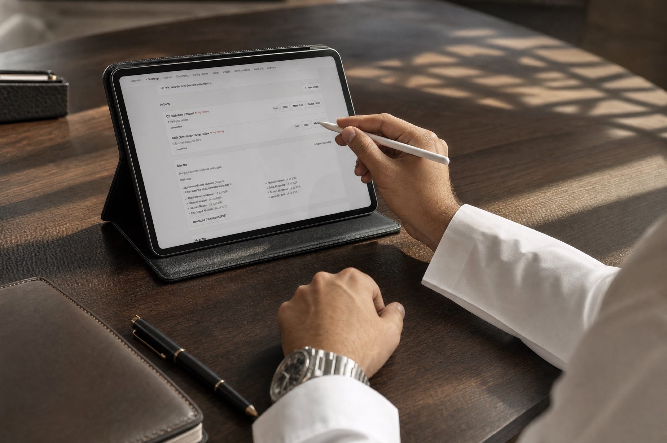 A person in a white shirt signs board minutes on a tablet with a stylus at a dark wood table.